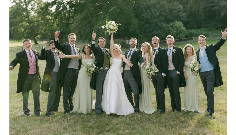 Bride and groom pose cheerfully with bridal and groom party in Hampshire country wedding venue garden.