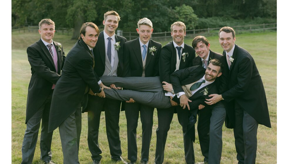 Groom's party in matching morning suits hold the groom in the Hampshire garden.