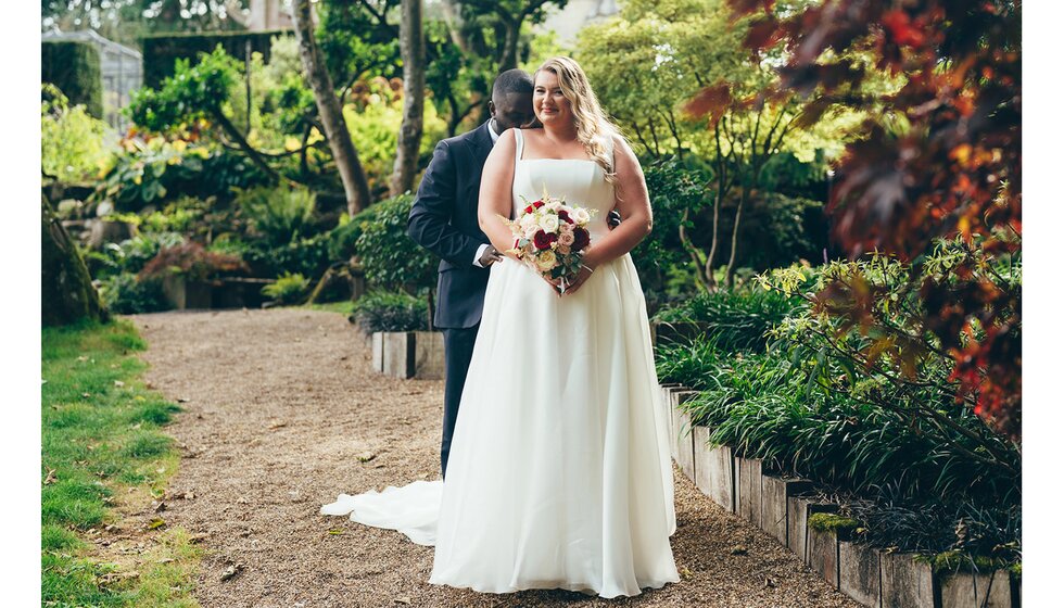 The bride wearing a corset wedding dress from Suzanne Neville poses in a Sussex garden with the groom.