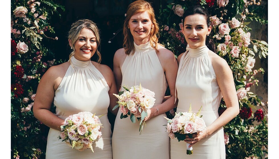 Bridesmaids holding small bouquets wear Maids to Measure champagne halter neck bridesmaid dresses