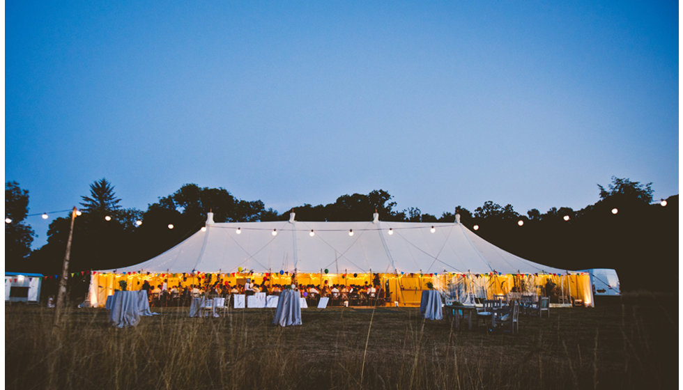 The marquee at dusk, lit by festoon lighting strung up outside.