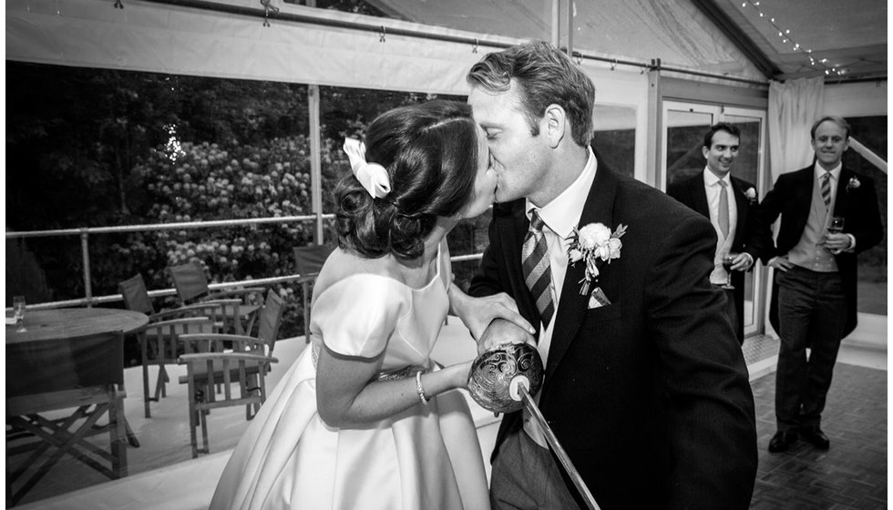 Min and Duncan share a kiss as they cut their wedding cake with a sword.