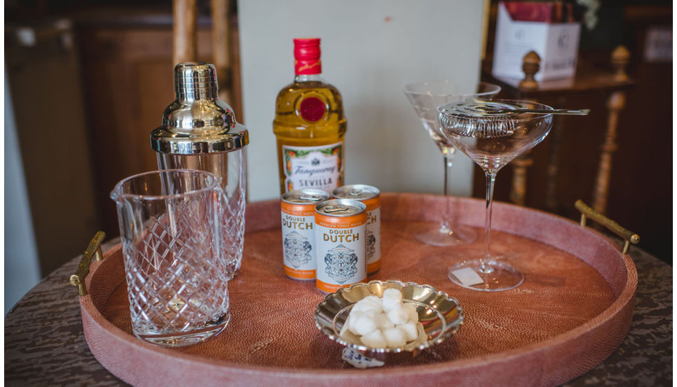 A cocktail tray styled with cut crystal glassware, cocktail glasses, a shaker, gin and tonics and sugar lumps in a silver bowl. 