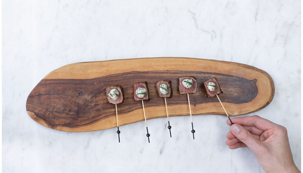 Seared beef slices with a dollop of horseradish cream served on a wooden board.