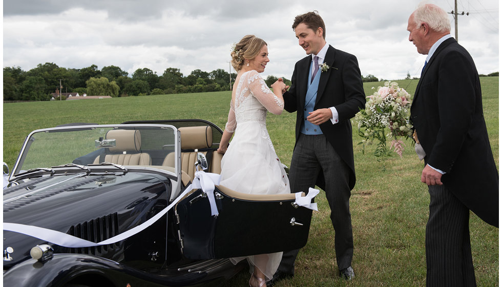 The groom helping the bride out the vintage car.