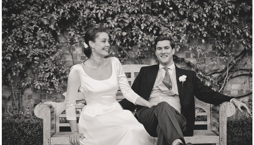 The bride and groom on a bench outside.