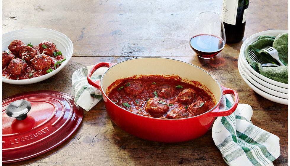 An oval cerise Le Creuset casserole dish with meatballs inside. 