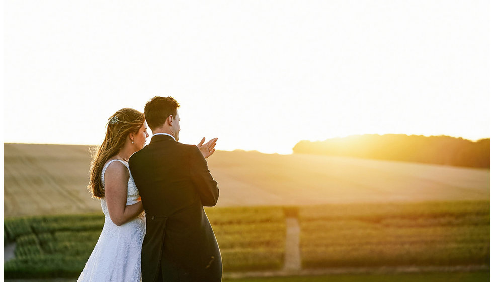 The bride and groom looking into the golden light over the countryside.