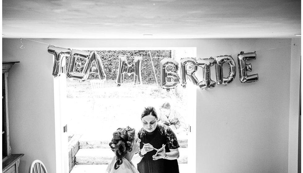 The bride having her make up done with balloons spelling team bride in the background.