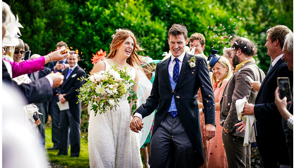 Josh and Victoria leave the Church holding hands. Their guests throwing confetti as they pass.