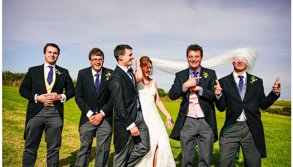 Brides veil blows in the wind to cover one of the ushers faces.