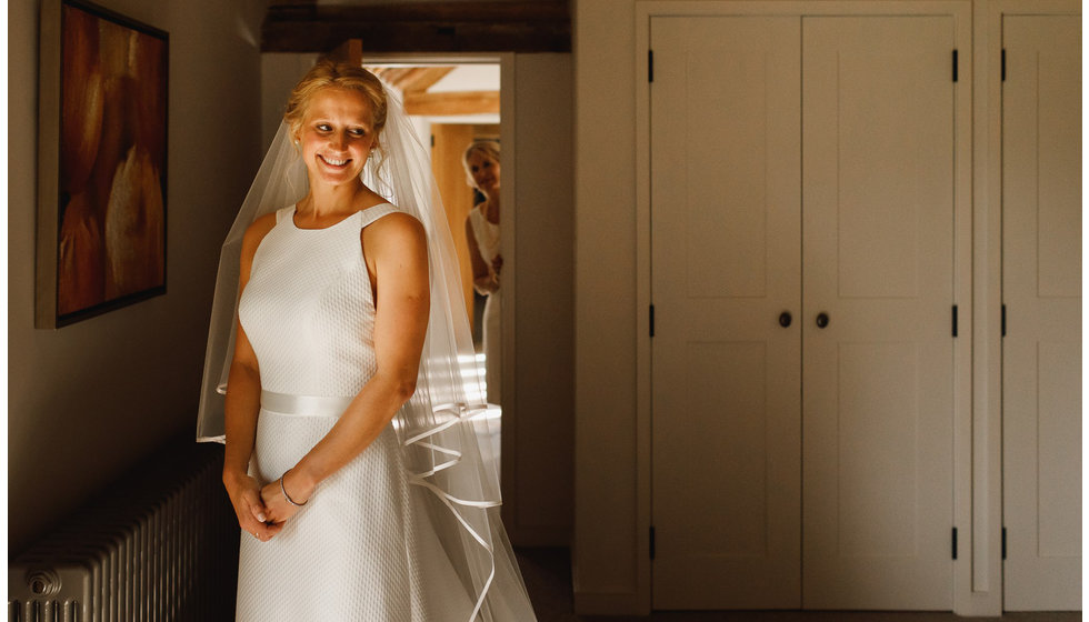 The bride stands in her wedding dress with her veil on.