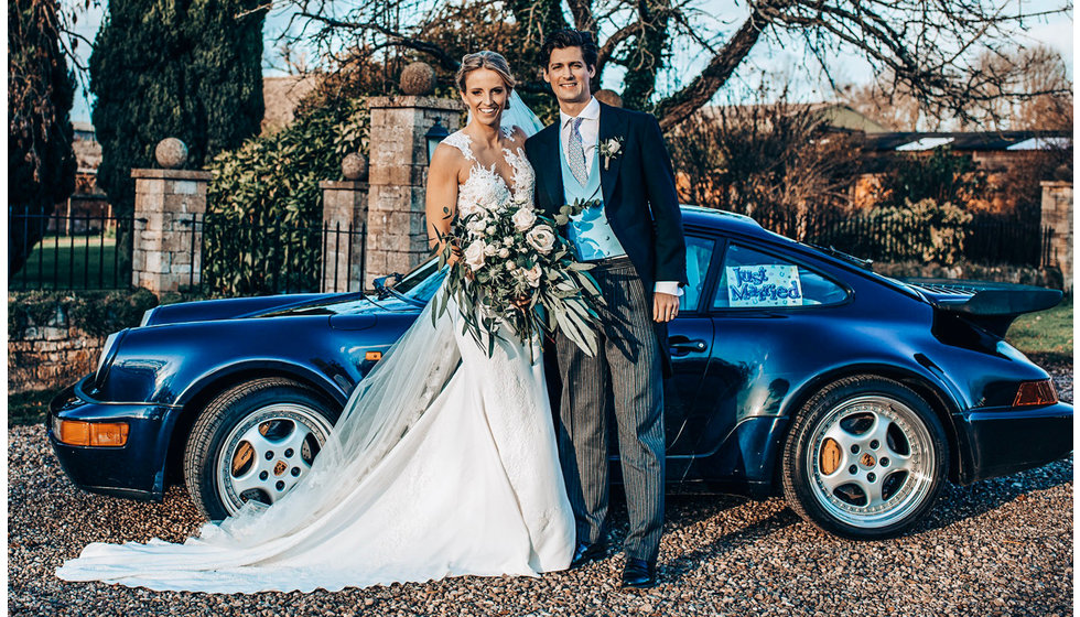 The bride and groom standing in front of a porsche.