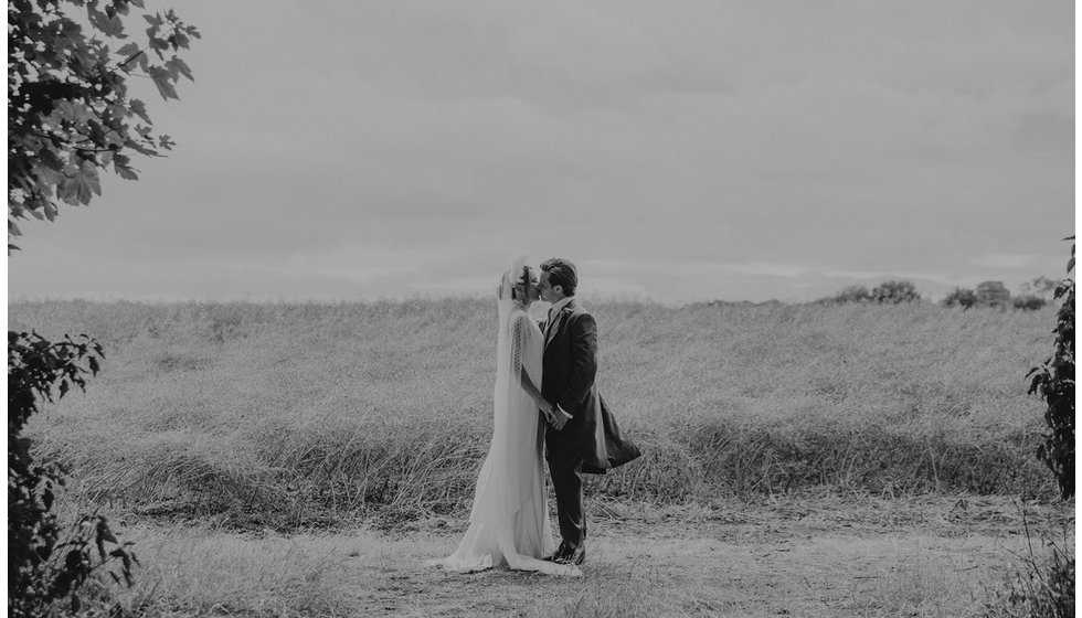 The bride and groom share a kiss in the field.