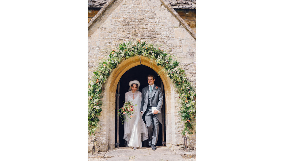 The bride and groom leaving the Church, walking under the beautifully decorated archway in flowers.