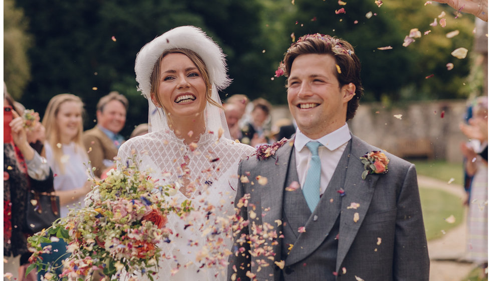 The bride and groom smile as they leave the Church walking through the confetti their guests throw in the air.