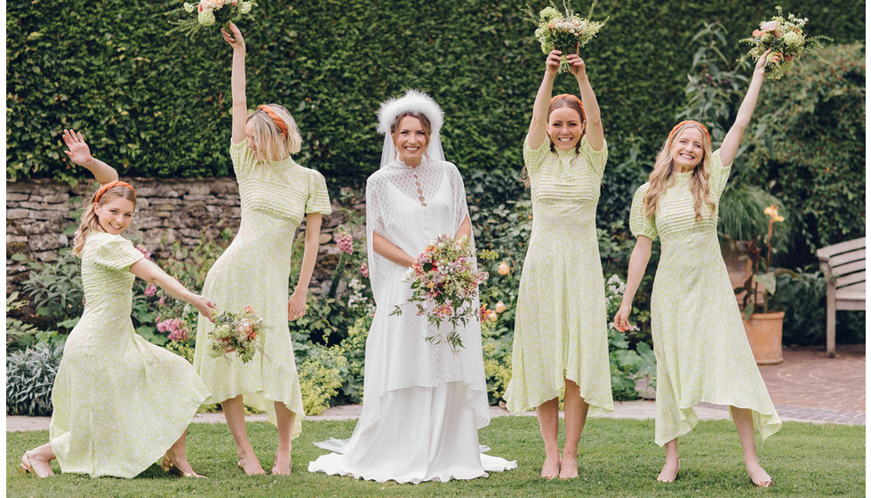 The bride and bridesmaids all pose around the bride holding their bouquets in the air.