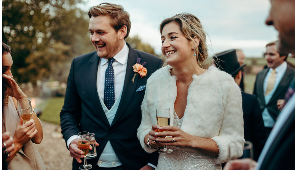 The bride and groom holding champagne talking to their guests at their wedding.