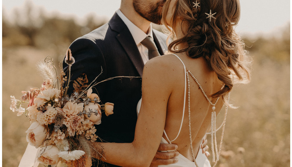 Louise wears a spaghetti strap wedding dress, stars in her hair and carried a boho bouquet of muted colours.