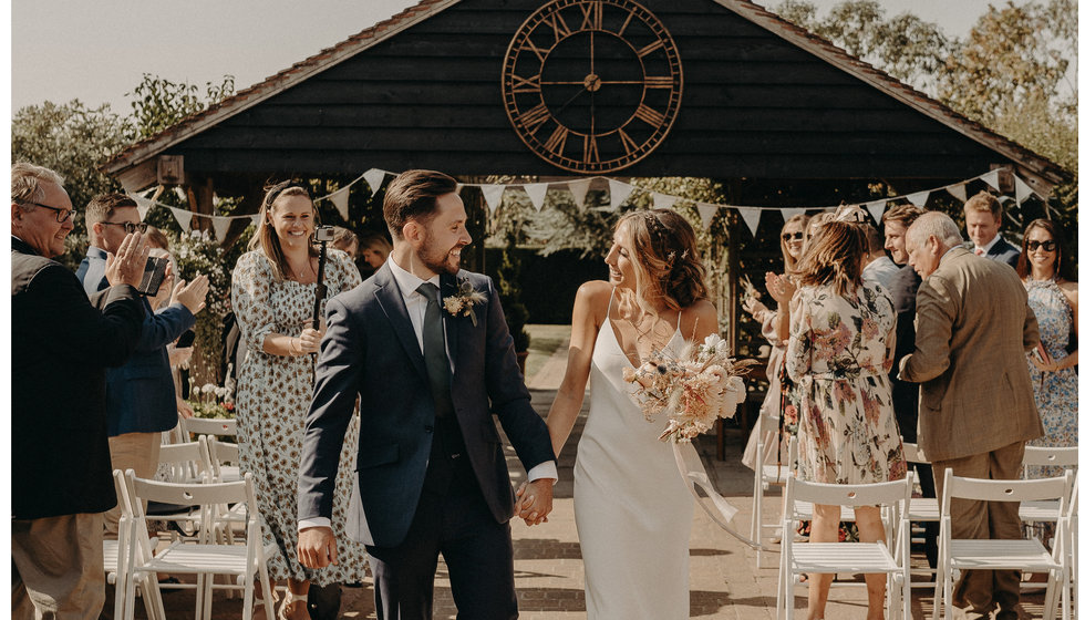 Matthew and Louise walking down the aisle of their outdoor intimate wedding with 22 guests in the September sunshine.