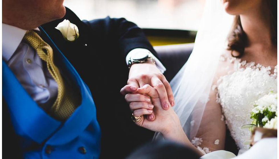 The bride and groom holding hands in the back of a yellow NYC cab. 