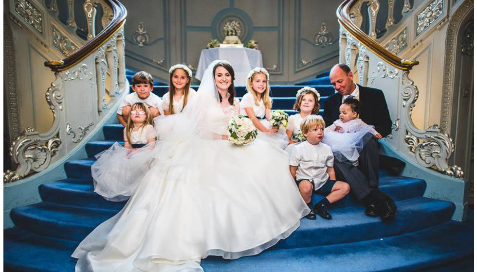 The bride her flower girls, and page boys sitting on the steps inside the Savile Club in London.