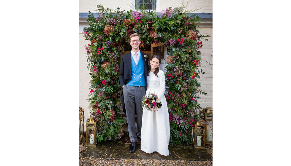 Edwina and Edward outside Edwina's parents house with a beautiful floral arch. 