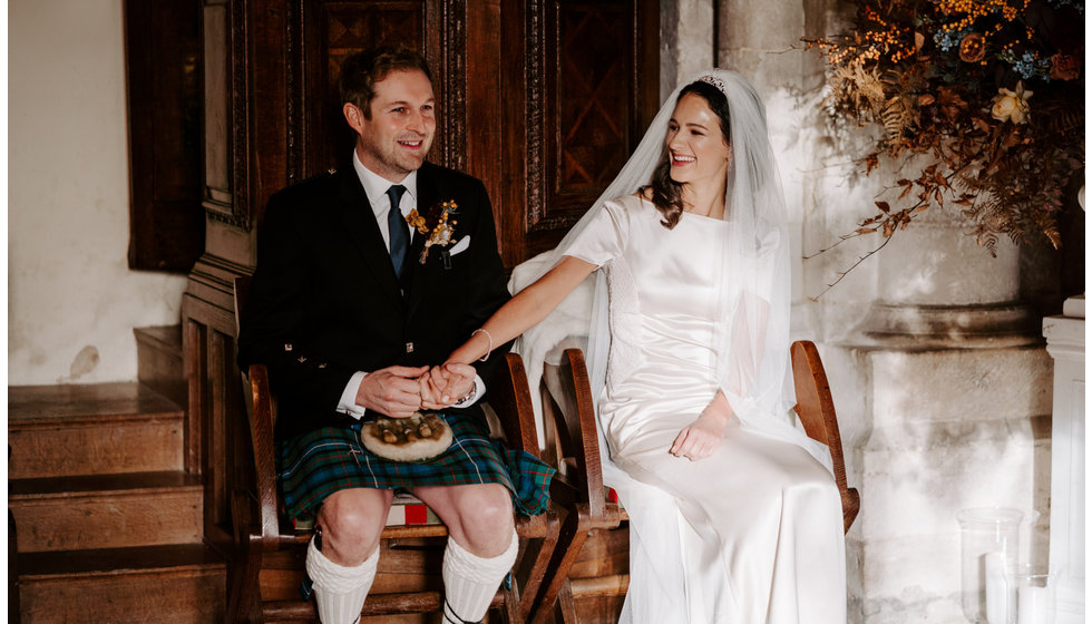 Sophie and Graeme sitting down holding hands in the Church during their intimate wedding ceremony.