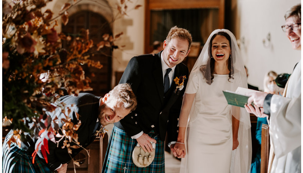 Sophie and Graeme laughing holding hands at the alter next to the vicar during their intimate Hampshire wedding.