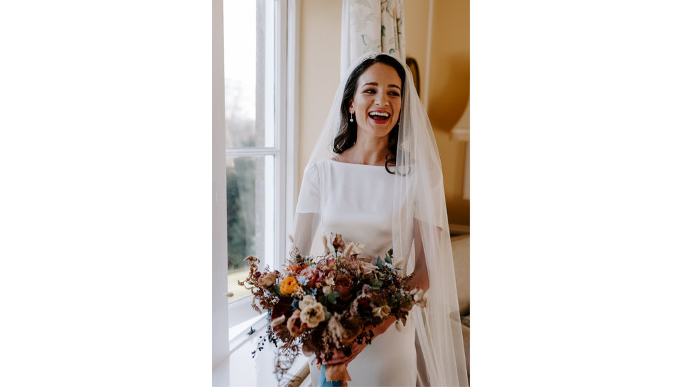 Sophie wearing her bespoke silk white short sleeves wedding dress and a veil. She holds her bouquet.