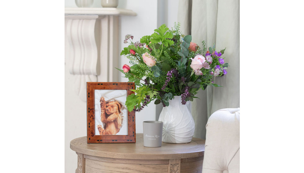 A table of a wooden frame a vase with flowers and a candle.