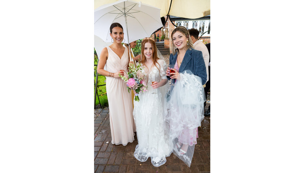 Bride Sarah stands with one of her guests and a bridesmaid outside on her wedding day.