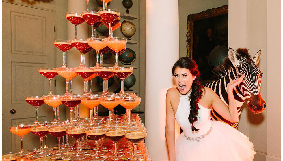 A bride stands next to a tower of espresso martinis. 