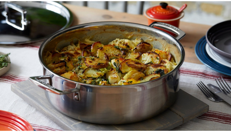 A large stainless steel deep pan filled with potatoes on a marble slab on a table. 