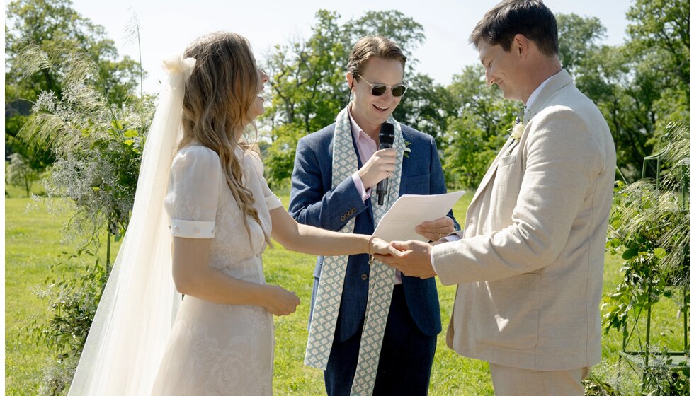 Charlotte & Harry's Magical Meadow Marquee Wedding in Oxfordshire: Bride and groom laughing during their sun-lip open-air ceremony with wedding celebrant