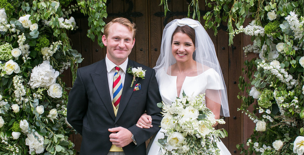 The couple posing in front of a beautiful flower arch in front of the church where they got married. 