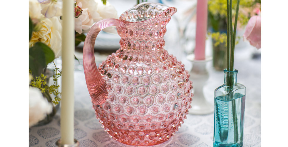 Pink hobnail jug on a table laid with flowers and candles.