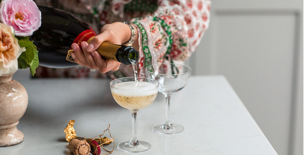 A magnum of champagne being poured into two champagne coupes.