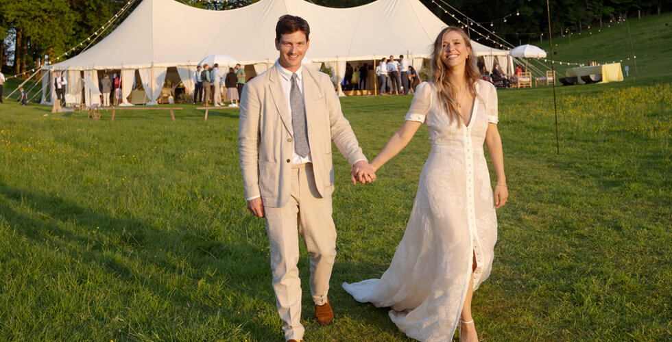 Sailcloth Marquee Wedding in Oxfordshire | A happy bride and groom walking in front of their wedding marquee on the sunlit meadow in Cotswolds